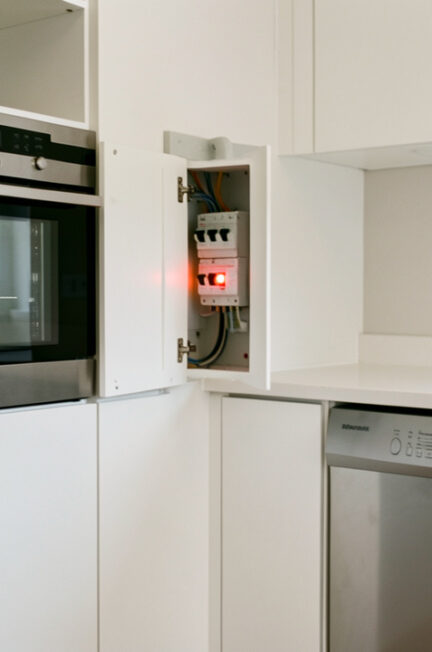 Cuisine moderne avec un four, un lave-vaisselle et un tableau électrique ouvert montrant un disjoncteur abaissé pour illustrer un diagnostic.