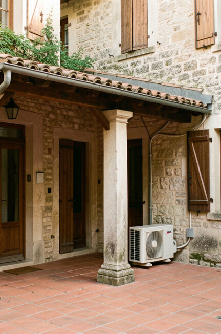 Ancienne maison française en pierre avec une unité extérieure de climatisation discrètement installée dans une cour intérieure végétalisée.